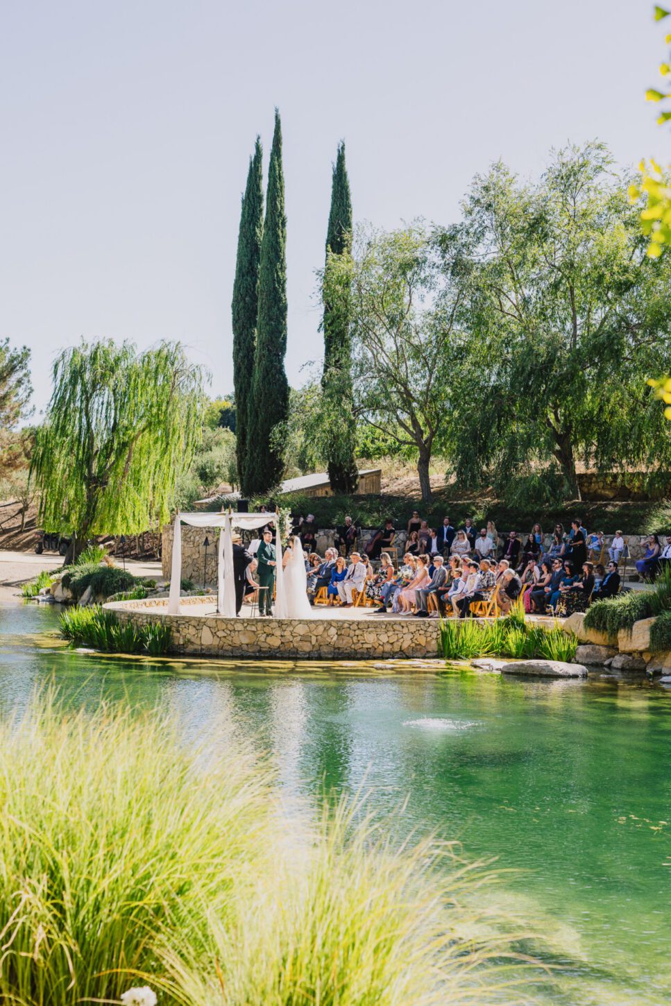 a view of the ceremony across the pond at a Terra Mia Summer Wedding