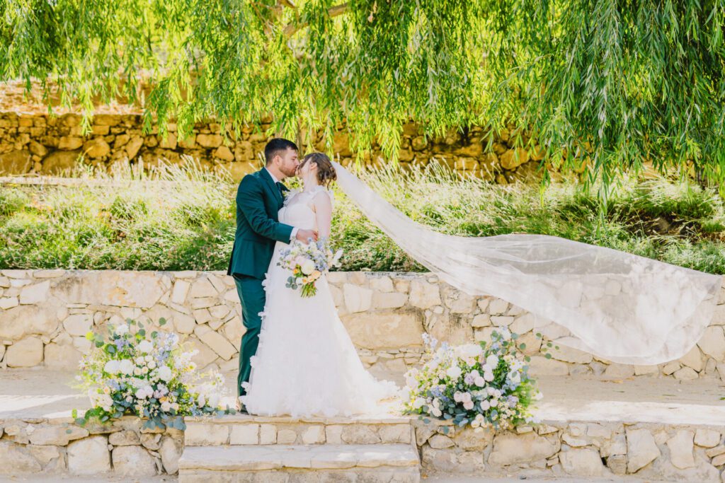 Bride and groom kiss with a veil flowing at a terra mia summer wedding