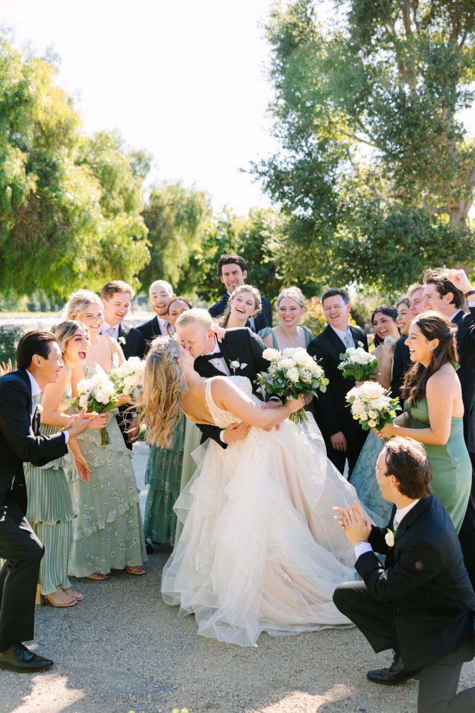 a bride and groom share a kiss in front of their wedding party at The White Barn
